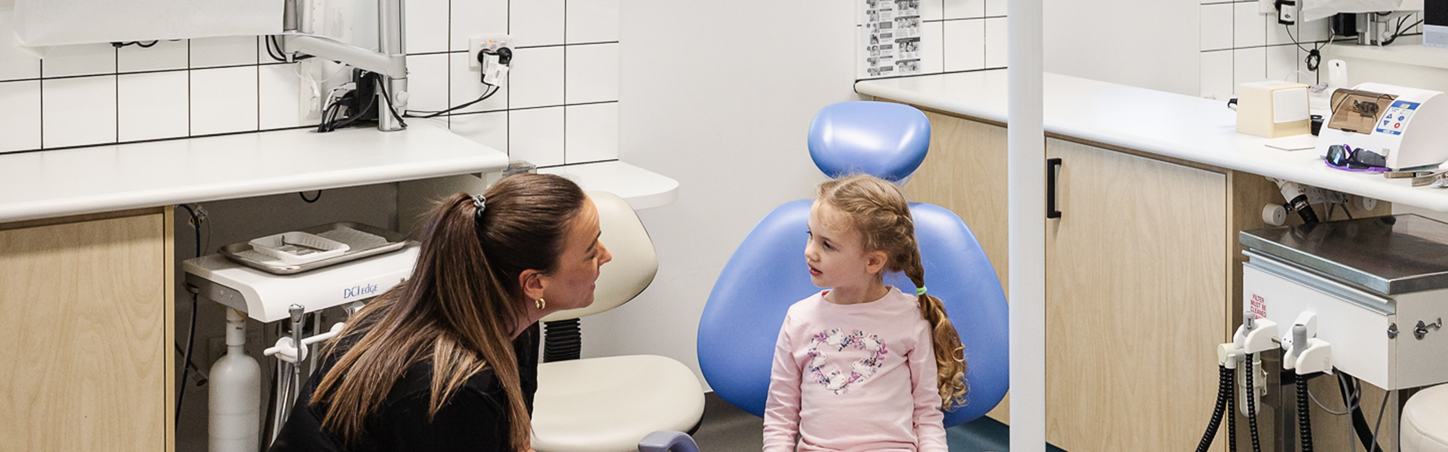 A young girl sitting in a dental chair listening to a female dentist who is crouched low near the dental chair